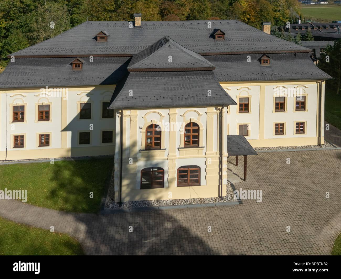 Vue aérienne de la façade jaune pâle du Dolny Kastiel contrastant avec son toit sombre, sur fond de feuillage d'automne, Necpaly, région de Zilina Banque D'Images