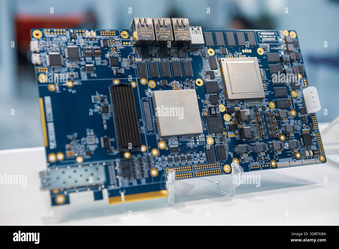 Une carte de circuit imprimé bleue sophistiquée avec divers micropuces, condensateurs et connecteurs plaqués or est affichée sur un support blanc Banque D'Images