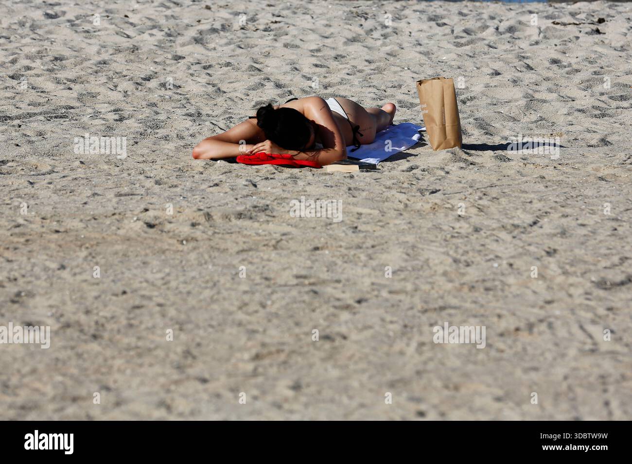 Geelong, Australie. 18 décembre 2025. Une femme est allongée sur le sable en train de bronzer à Geelong Beach par temps chaud. Les gens se rassemblent à Geelong Beach alors que Victoria subit une chaleur extrême, Melbourne atteignant un maximum de 36 °C aujourd'hui. Les conditions chaudes devraient se poursuivre, Melbourne devrait atteindre environ 33 °C demain. Le Bureau of Meteorology a émis un avertissement de vague de chaleur grave pour Victoria, conseillant aux résidents de rester hydratés, de limiter l'exposition au soleil et de suivre les directives sur la chaleur et la santé. Crédit : SOPA images Limited/Alamy Live News Banque D'Images