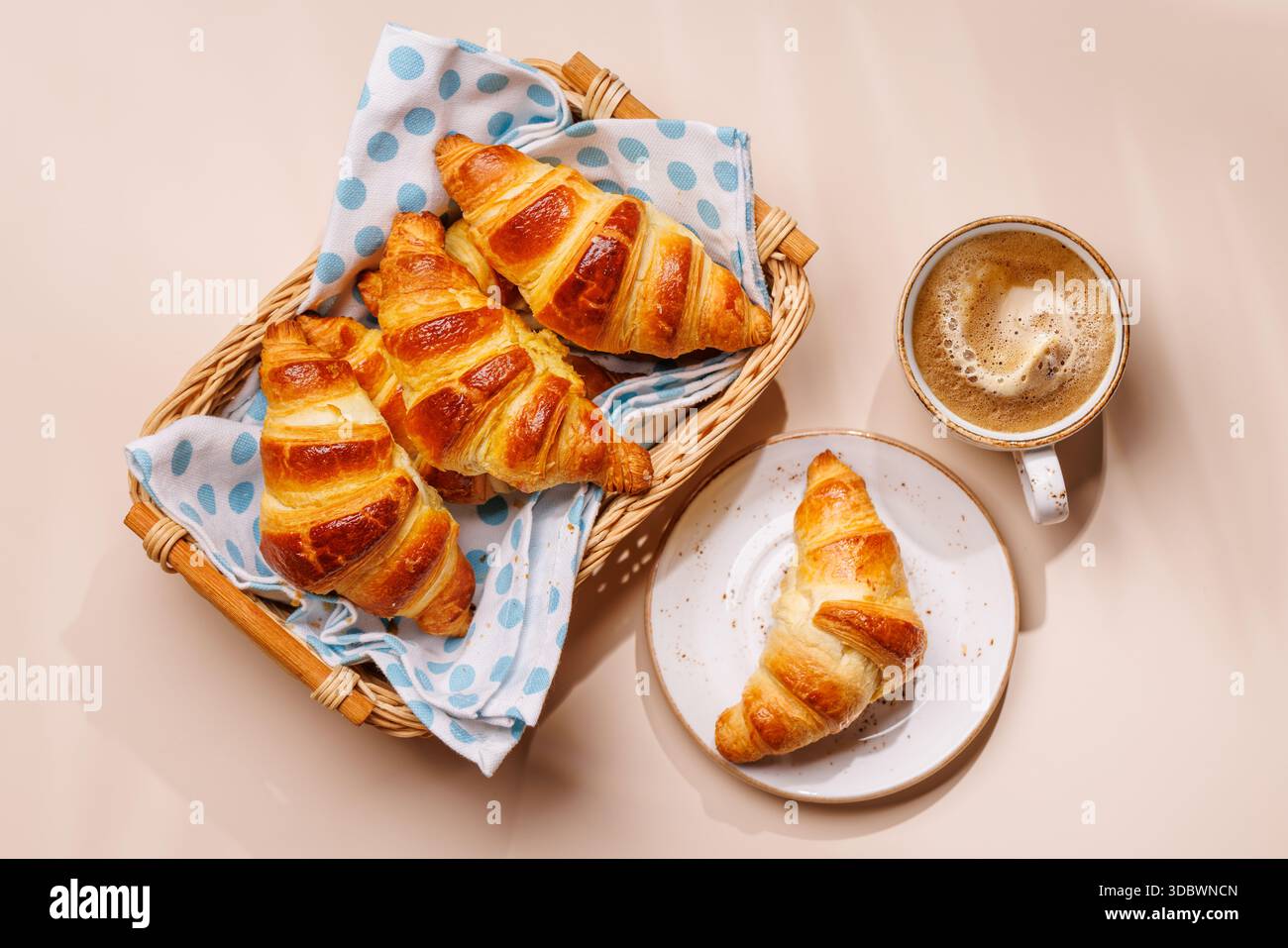 Croissants aromatiques dans un panier en osier avec tasse de café sur fond clair, scène de petit déjeuner confortable Banque D'Images