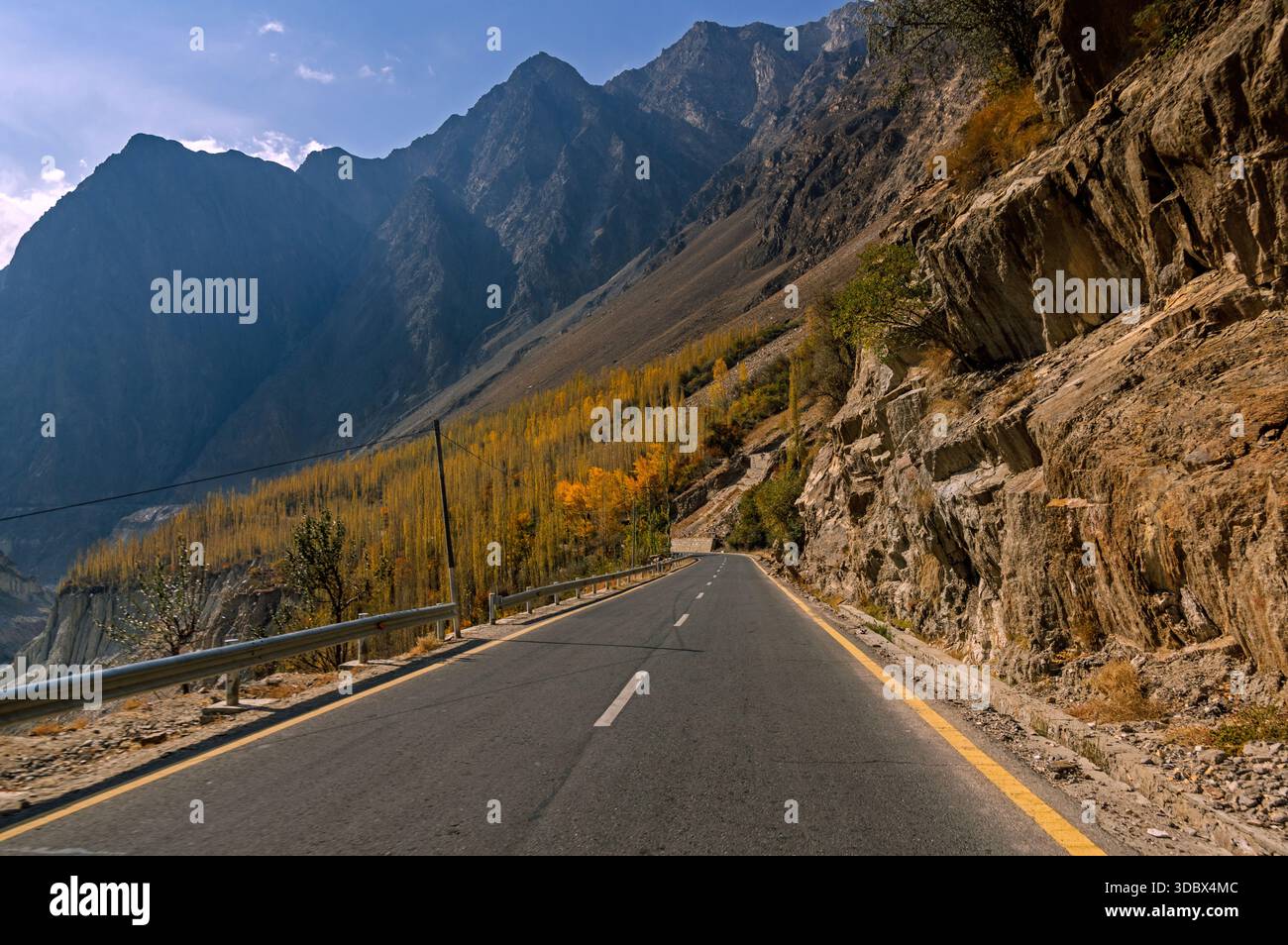 Vue d'une longue route coupant à travers des montagnes escarpées avec quelques arbres colorés d'automne accrochés aux pentes abruptes, Hunza, Gilgit Baltistan, Pakistan. Banque D'Images