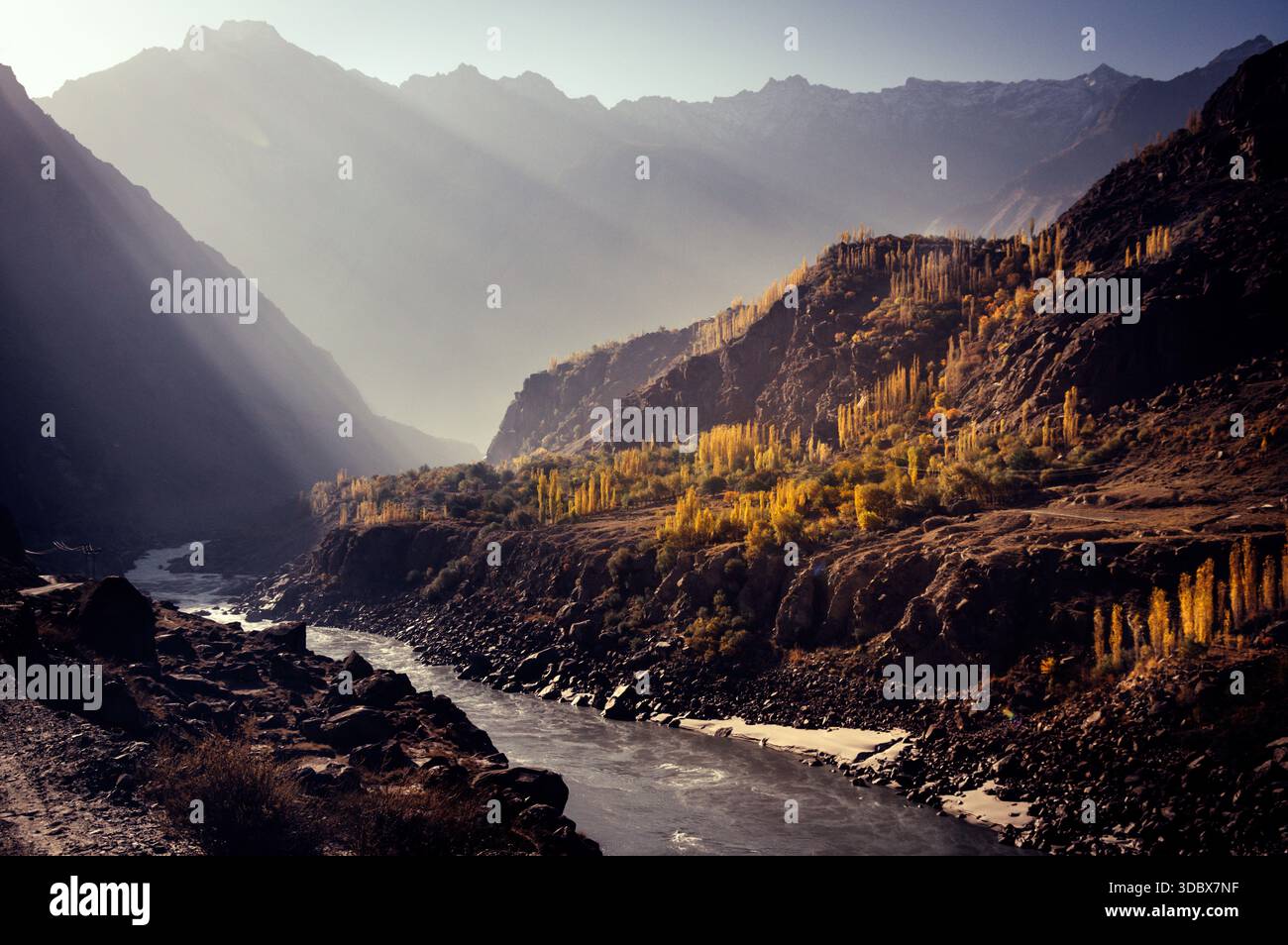 Vue sur une rivière serpentant à travers un terrain accidenté et rocheux, avec des arbres dorés accrochés aux collines sous le regard vigilant des montagnes lointaines, Jaglo Banque D'Images
