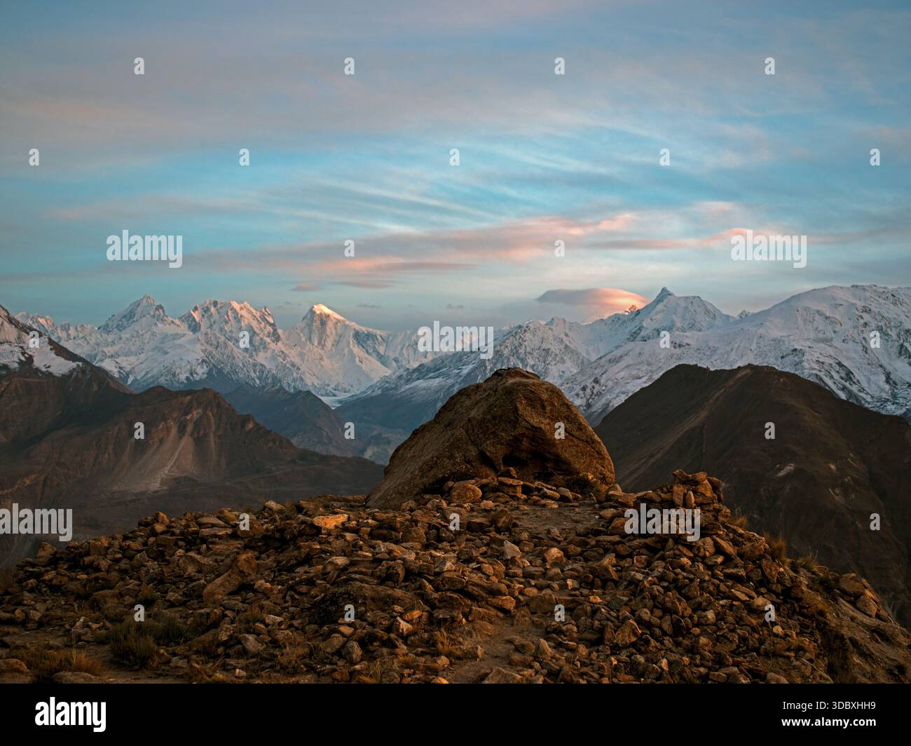 Vue sur un terrain accidenté et rocheux mène à des sommets enneigés sous un ciel pastel, un contraste frappant entre la terre et le ciel, Hunza, Gilgit Baltistan, Paki Banque D'Images