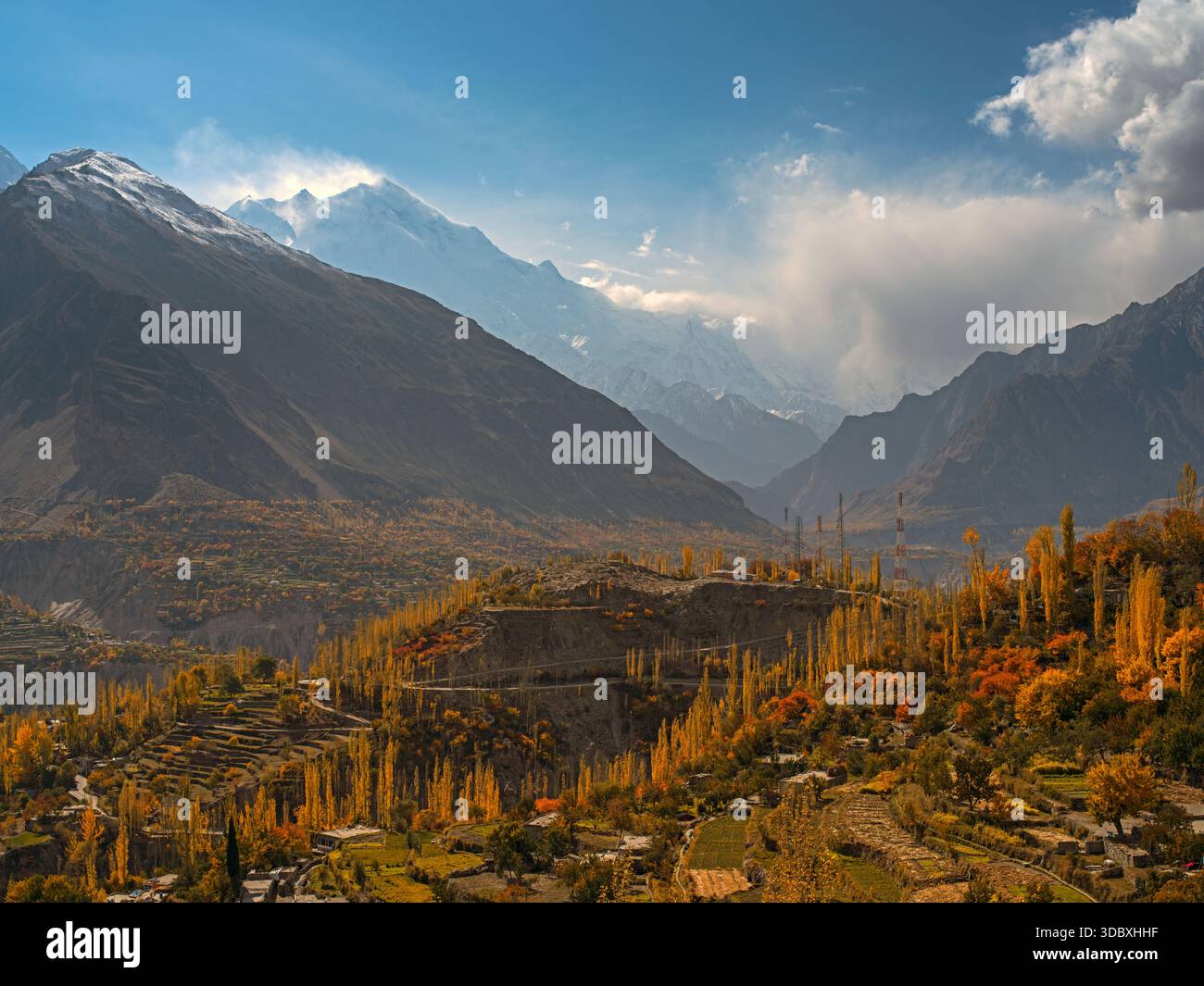 Vue d'arbres d'automne dorés accrochés aux pentes sous les imposantes montagnes enneigées sous un ciel lumineux, Hunza, Gilgit Baltistan, Pakistan. Banque D'Images