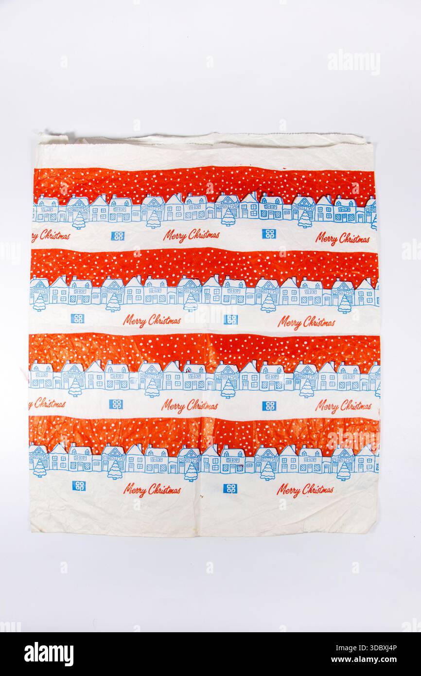 Sac en papier vintage festif rouge et blanc coopératif avec des dessins au trait bleu de maisons enneigées, d'arbres et un texte joyeux Noël dans des bandes horizontales répétées Banque D'Images
