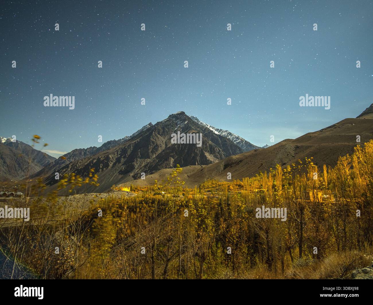 Vue d'une chaîne de montagnes imposante sous un ciel étoilé, avec des arbres d'automne dorés bordant la vallée à Gupis, Gilgit Baltistan, Pakistan. Banque D'Images