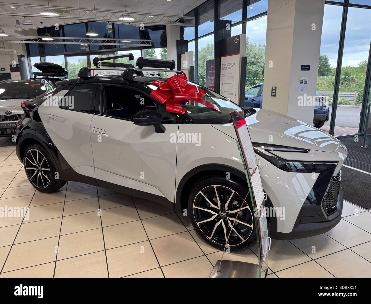 WIRRAL, CHESHIRE, ANGLETERRE - 27 JUIN 2025 : une vue montre une voiture neuve avec arc rouge exposée dans un showroom de voiture à vendre - Image de stock capturée avec un smartphone