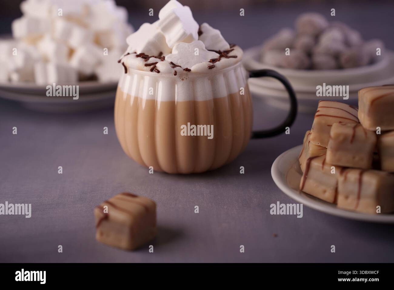 mug confortable de chocolat chaud garni de crème fouettée et de saupoudrées de chocolat, entouré de plaques de guimauves et de morceaux de fudge arrosés sur un doux Banque D'Images