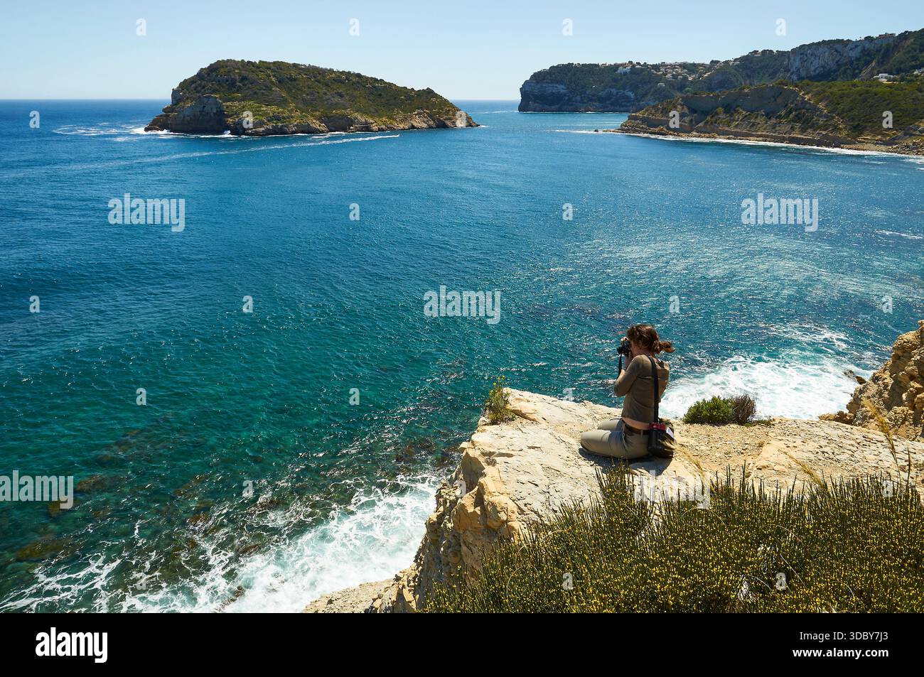 Photographe femme photographiant depuis les falaises dans le sentier de randonnée SL-CV 98, avec l'île de Portitxol en arrière-plan (Portichol, Jávea, Alicante, Espagne) Banque D'Images