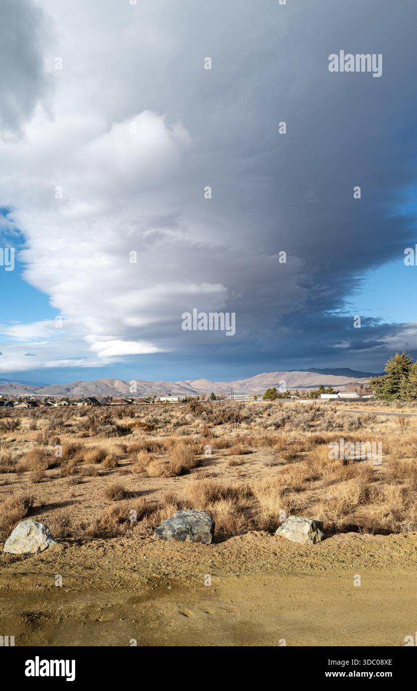 Vue verticale de trois rochers dans un paysage désertique avec un nuage blanc spectaculaire et tourbillonnant pilier sous un ciel bleu ensoleillé. Banque D'Images