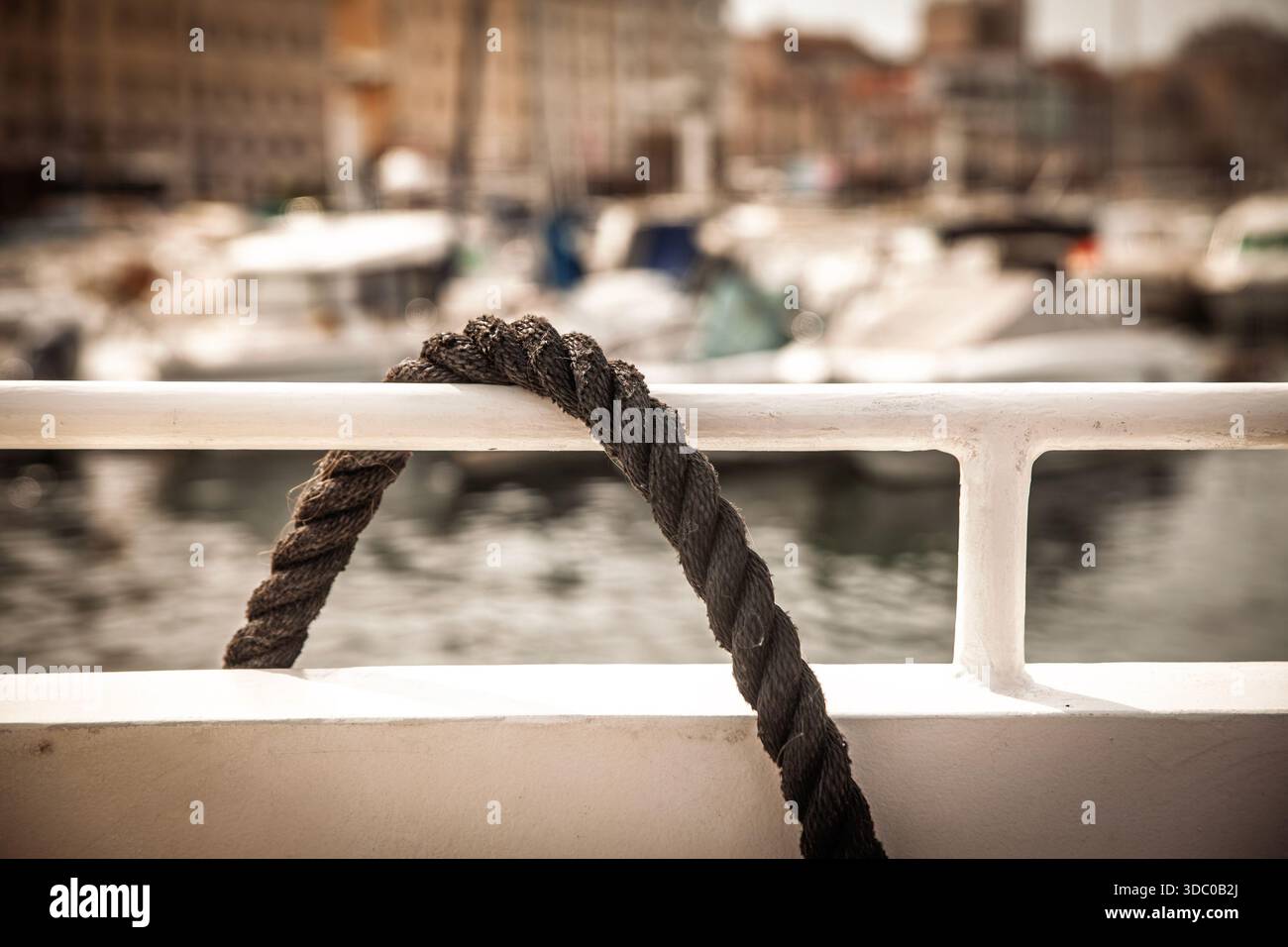 Épaisse ligne d'amarrage à trois brins drapée sur un rail blanc dans une marina. La corde forme une boucle contre un port flou, illustrant l'utilisation de la ligne de quai pour s Banque D'Images