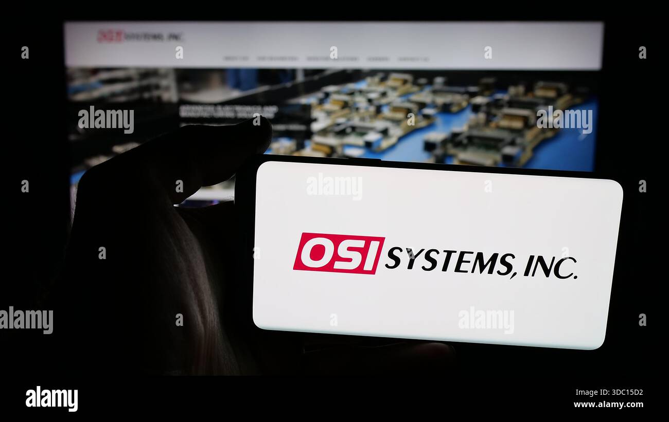 Dans cette illustration photo, une personne tient un téléphone portable avec le logo de la société de sécurité américaine OSI Systems Inc sur l'écran devant la page Web. Banque D'Images