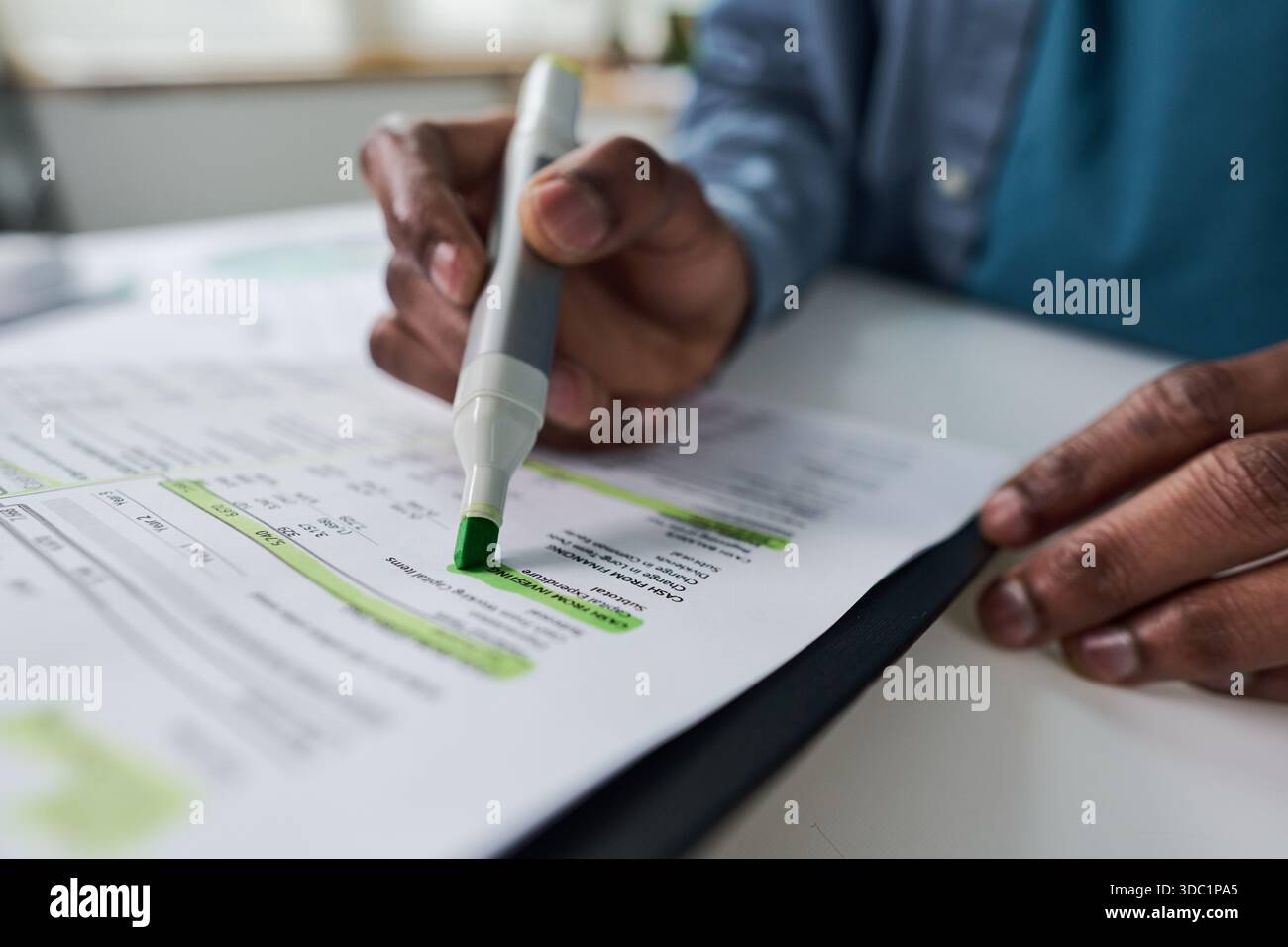 Homme noir mettant en évidence les données financières sur le document imprimé avec marqueur vert, se concentrant sur l'analyse des chiffres et la prise de notes, gros plan des mains travaillant au bureau dans le cadre du bureau Banque D'Images