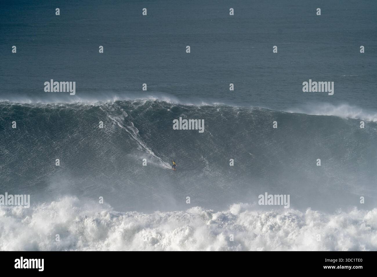 Surfeuse face à une puissante vague à Praia do Norte, Nazaré, Portugal. Emplacement emblématique de l'océan Atlantique pour le surf extrême des femmes. Banque D'Images