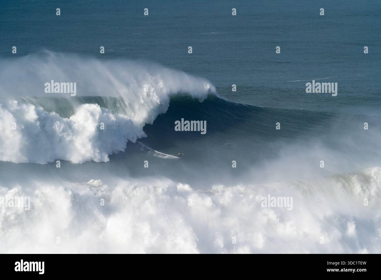 Surfeur face à une puissante vague à Praia do Norte, Nazaré, Portugal. Emplacement emblématique de l'océan Atlantique pour le surf extrême des femmes. Banque D'Images