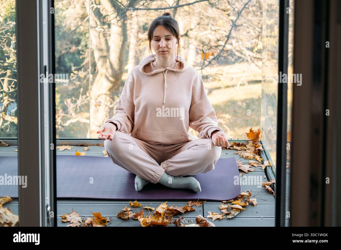La femme est assise les yeux fermés dans la pose méditative sur le balcon pendant l'automne. Solitude paisible, vie intentionnelle, espace mental, détox numérique. Banque D'Images