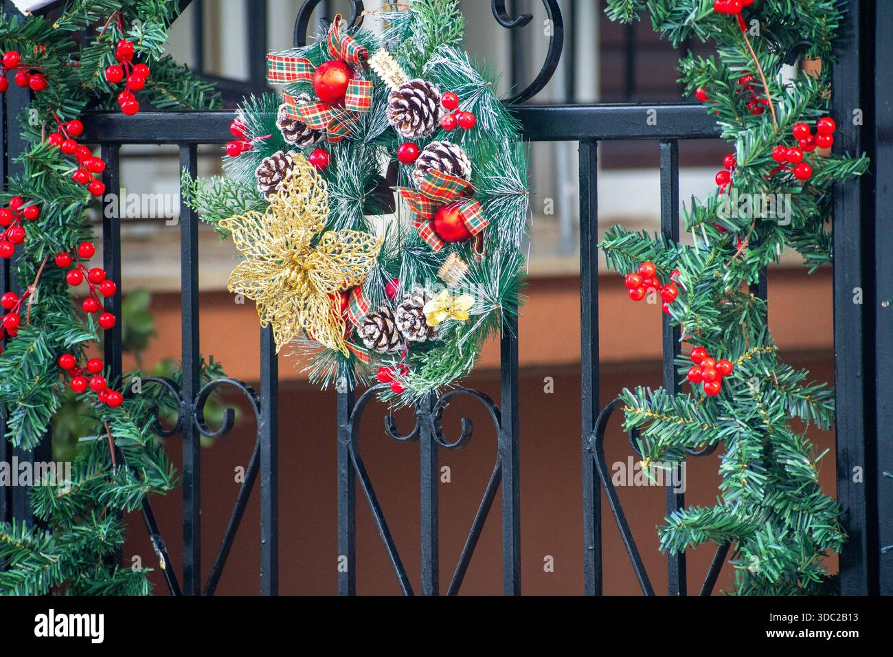 Couronne de Noël festive avec ornements rouges et fleur d'or accrochée sur une porte de fer noir Banque D'Images