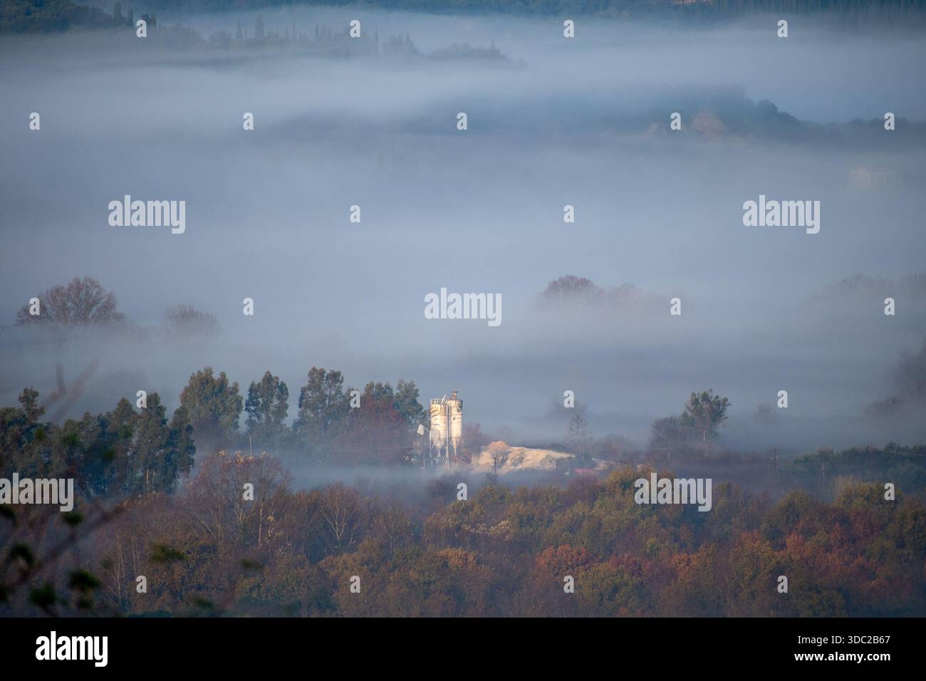 Silos industriels émergeant d'épais brouillard matinal dans un paysage de vallée rurale à Corfou Banque D'Images