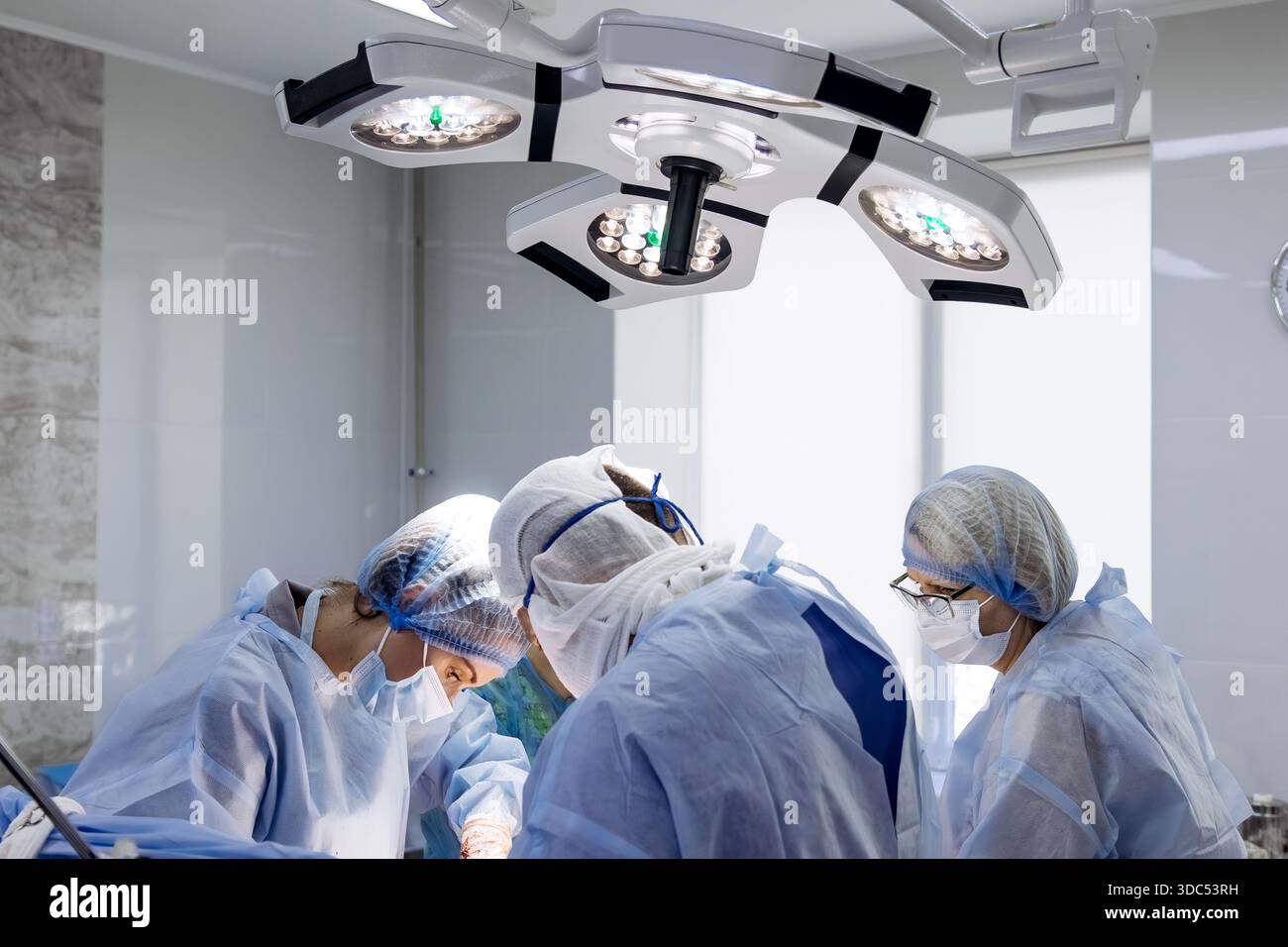 L'équipe chirurgicale dans les gommages bleus est engagée dans une procédure sous des lumières vives, mettant l'accent sur la collaboration et la compétence dans un setti médical propre et professionnel Banque D'Images