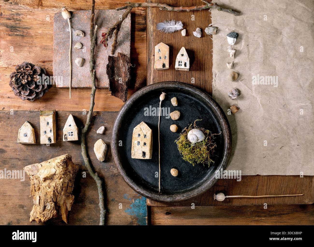 Composition rustique de conception créative plate avec des maisons miniatures en céramique, des galets, coquille, mousse, pomme de pin, plume, brindilles sur fond en bois. Natur Banque D'Images