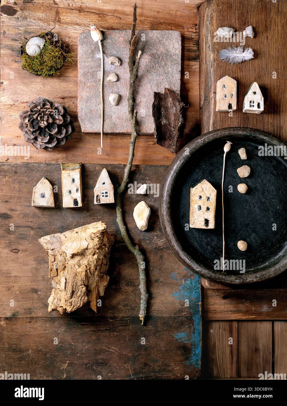 Composition rustique de conception créative plate avec des maisons miniatures en céramique, des galets, coquille, mousse, pomme de pin, plume, brindilles sur fond en bois. Natur Banque D'Images