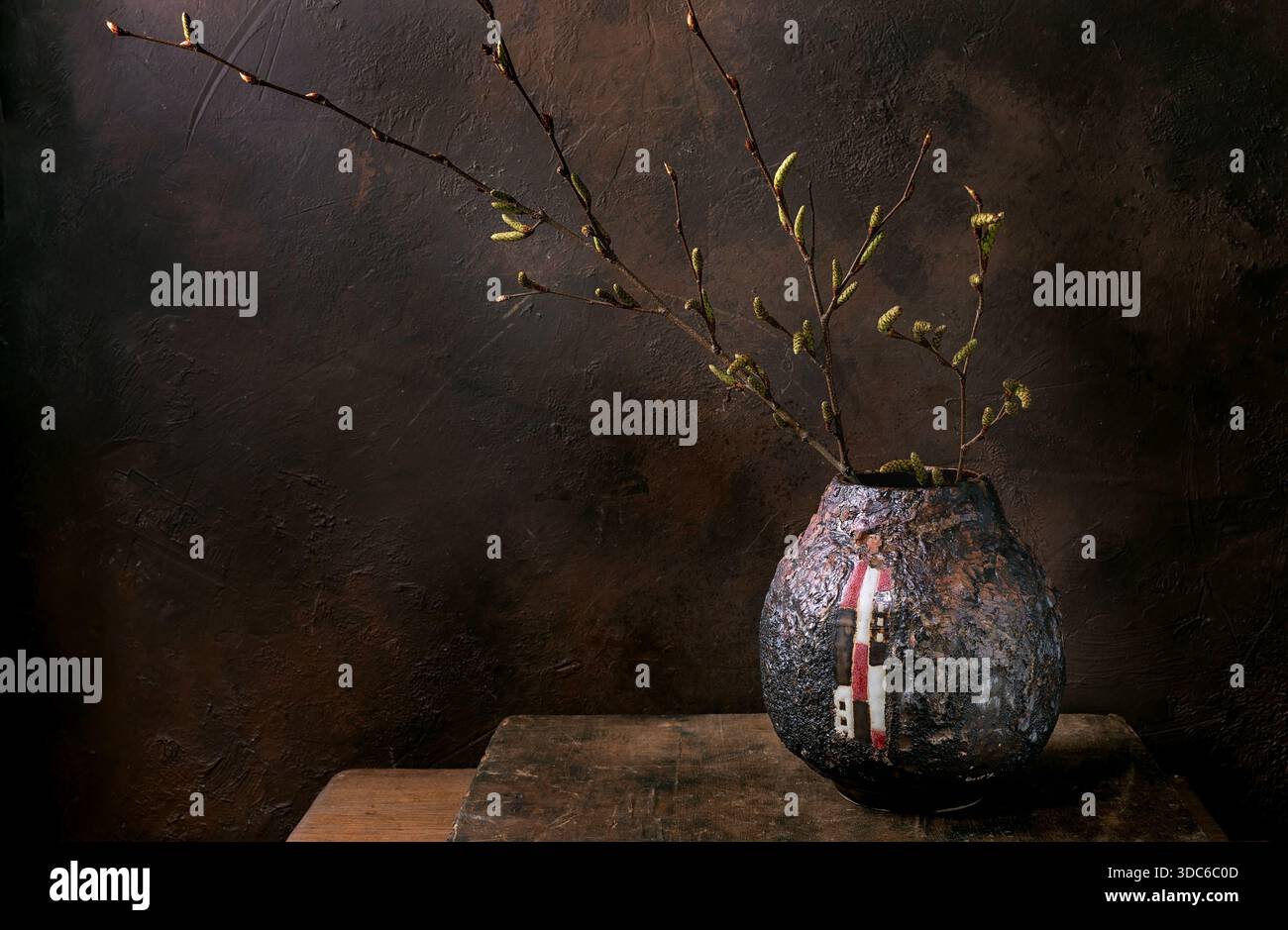 Nature morte artistique avec des branches de saule en fleurs dans un vase en céramique texturé contre un mur brun foncé. Composition minimaliste avec table en bois crée m Banque D'Images