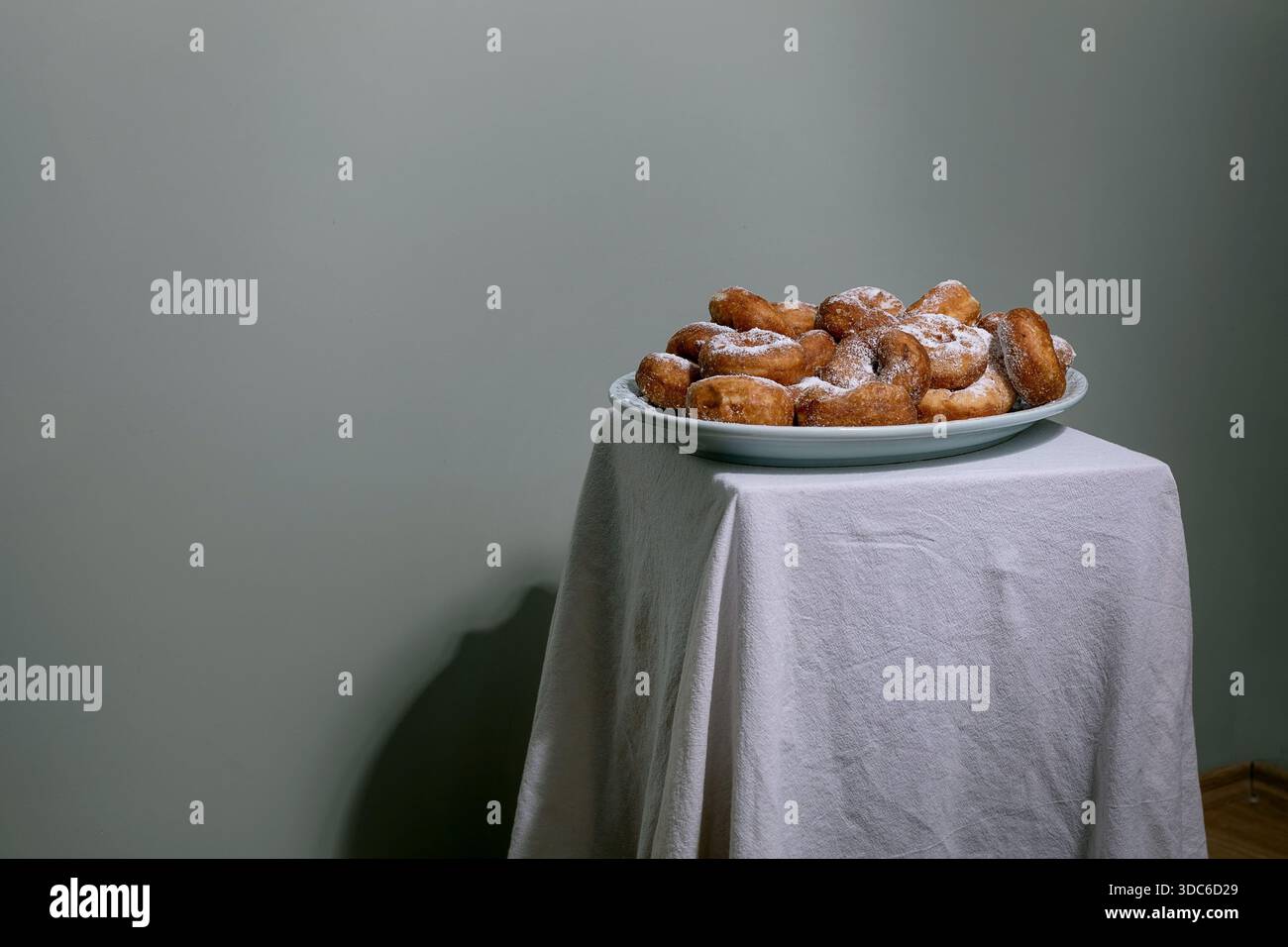 Beignets frais faits maison saupoudrés de sucre en poudre servis sur assiette bleue. Composition minimaliste avec nappe blanche sur fond neutre. Banque D'Images
