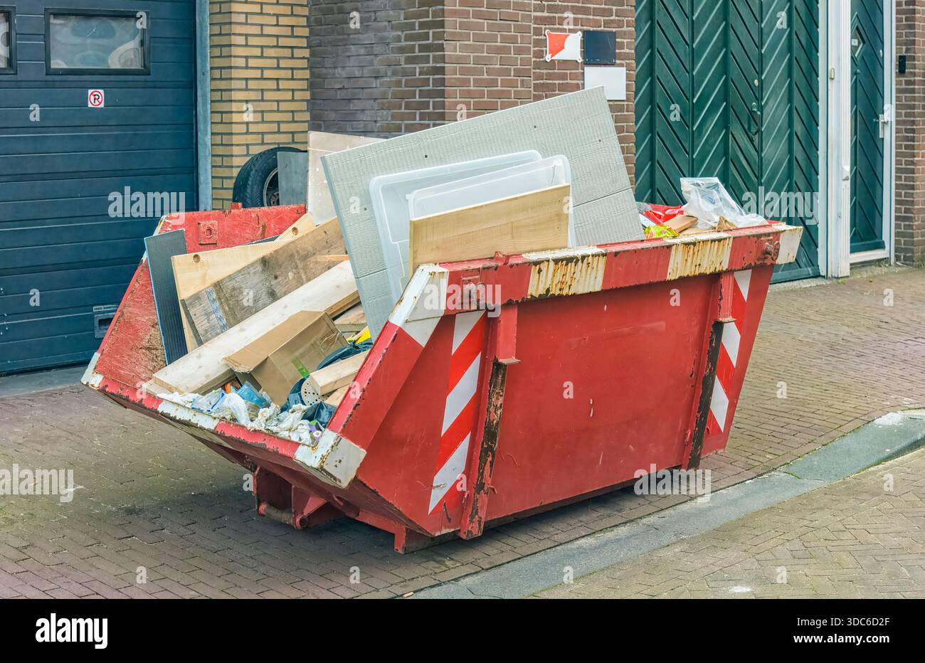 conteneur de déchets de construction rouge rempli de divers stands de déchets à l'extérieur sur la rue à côté d'un volet roulant d'un bâtiment Banque D'Images