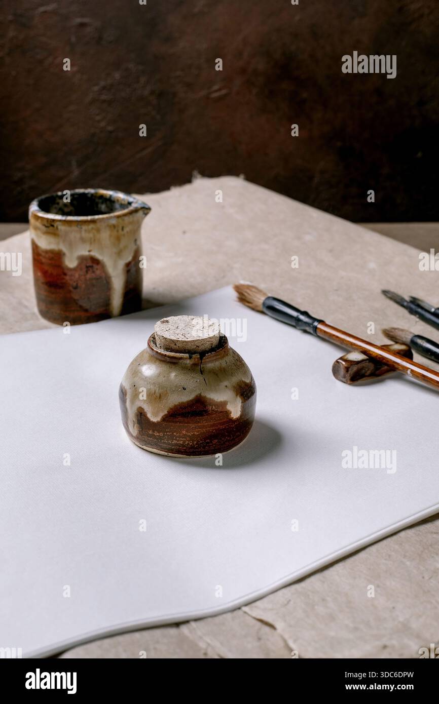 Pots et brosses en céramique faits à la main sur papier de riz blanc et de mûrier. Installation traditionnelle de studio de poterie avec des récipients vitrés rustiques et des outils de peinture Banque D'Images