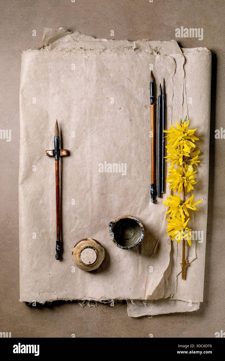 Vintage pinceaux calligraphie pot d'encre et fleurs de forsythia jaune sur fond de papier de mûrier fait à la main. Composition artistique à plat pour baguette créative Banque D'Images