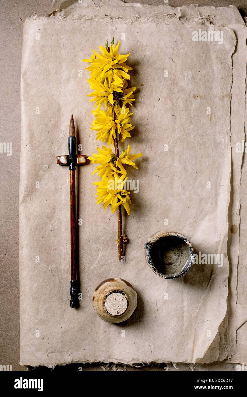 Composition artistique jaune forsythia branche calligraphie en bois pot d'encre stylo sur papier mûrier vintage. Esthétique minimale à plat pour un travail créatif spa Banque D'Images