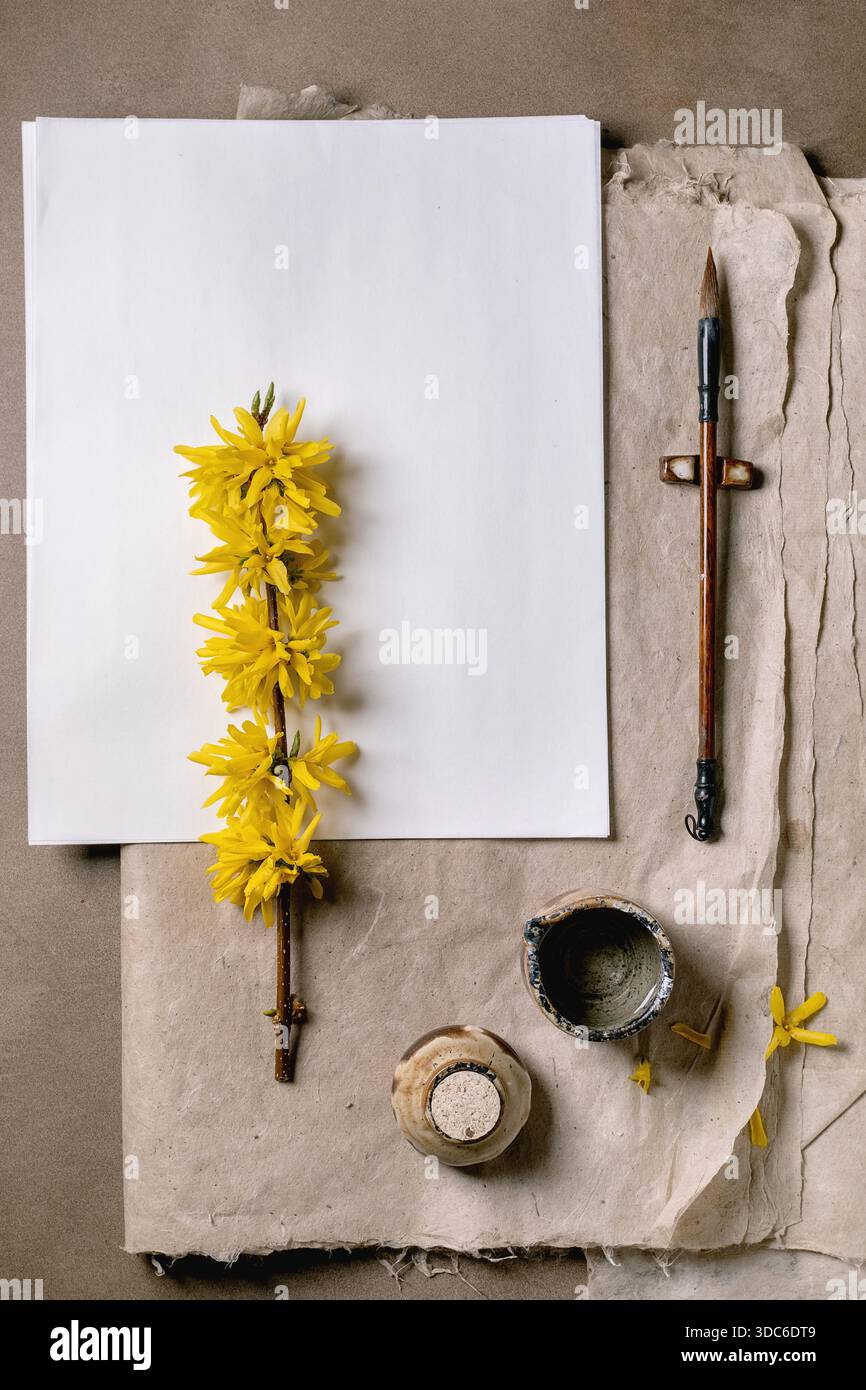 Espace de travail créatif avec riz blanc et papier mûrier jaune forsythia branche vintage pinceau petit récipient en céramique sur fond de papier fait à la main. S/O Banque D'Images