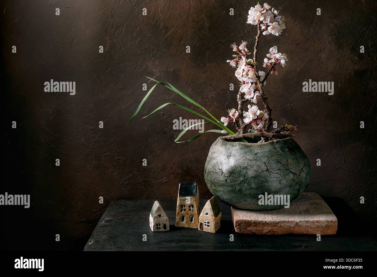 Élégant arrangement de natures mortes de style japonais ikebana avec pot en céramique avec branche de cerise fleurie petites maisons décoratives sur fond rustique sombre Banque D'Images