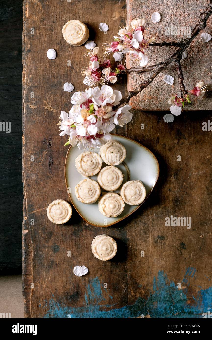 Bonbons à la crème de sésame faits maison sur plaque blanche avec floraison branche de fleur de cerisier. Fond en bois rustique avec des fleurs de printemps et de la pâtisserie. Vue de dessus St Banque D'Images