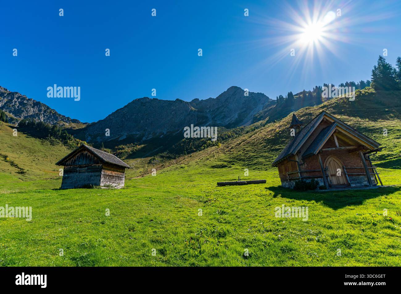 Deux charmants chalets en bois se dressent paisiblement sur des prairies verdoyantes, encadrées par des montagnes majestueuses sous la lumière du soleil, évoquant la tranquillité et natura Banque D'Images