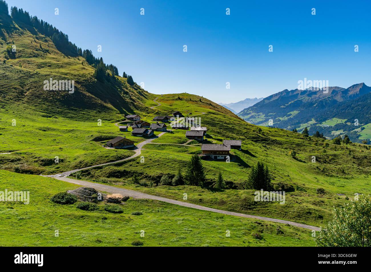 Une randonnée tranquille en montagne révèle de charmants chalets en bois nichés dans des prairies verdoyantes sous un ciel clair, évoquant la paix et l'aventure Banque D'Images