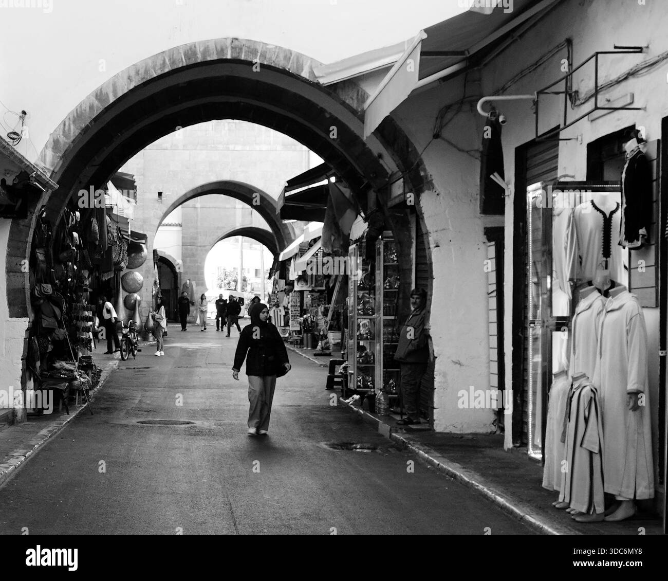 Les piétons se promènent sous des arches de pierre dans le quartier Habous de Casablanca, au Maroc, illustrant la vie urbaine quotidienne et l'architecture. Banque D'Images