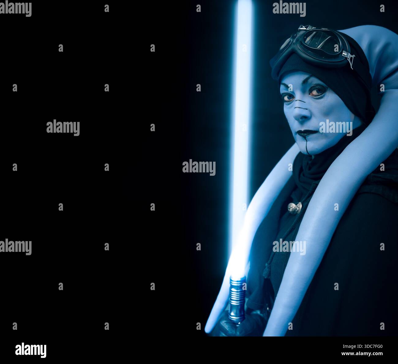 Gros plan portrait d'une fille cosplayer habillée en maître Jedi Star Wars Aayla Secura avec un sabre laser bleu et noir Banque D'Images