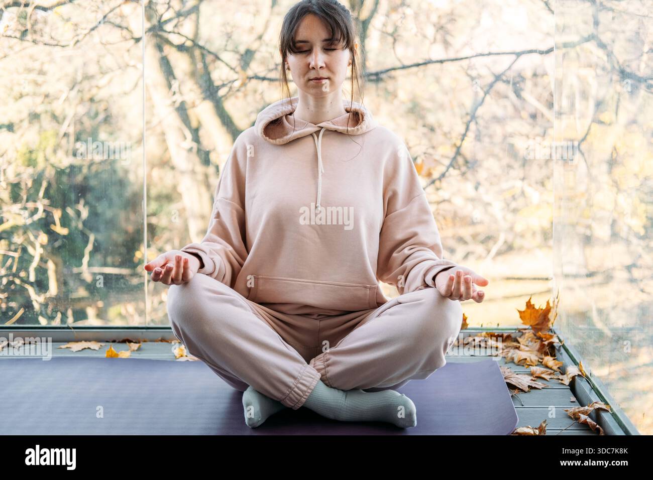 La femme est assise les yeux fermés dans la pose méditative sur le balcon pendant l'automne. Habitudes de soins personnels, sanctuaire de bien-être à domicile, style de vie tranquille. Banque D'Images