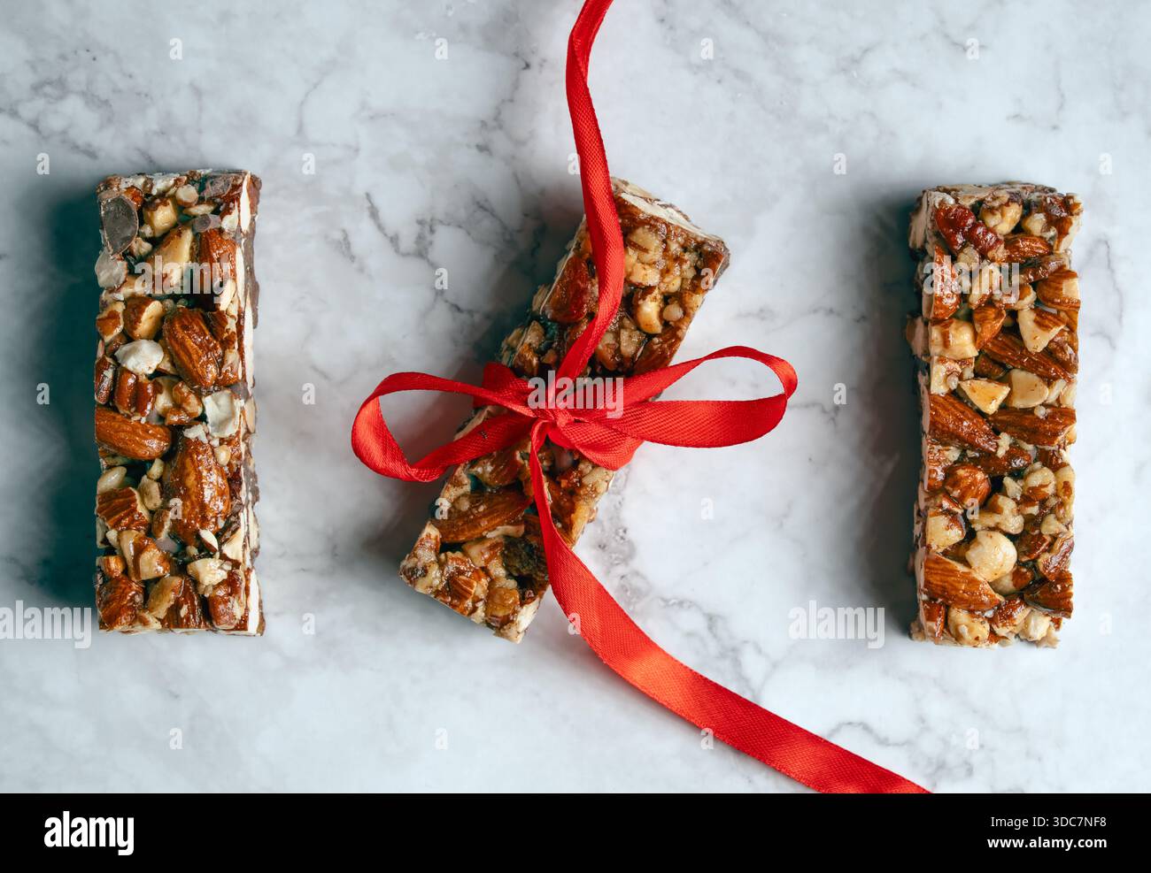 Trois barres gourmandes aux noix et au chocolat disposées sur une surface sophistiquée en marbre blanc, l'une attachée avec un ruban rouge décoratif Banque D'Images