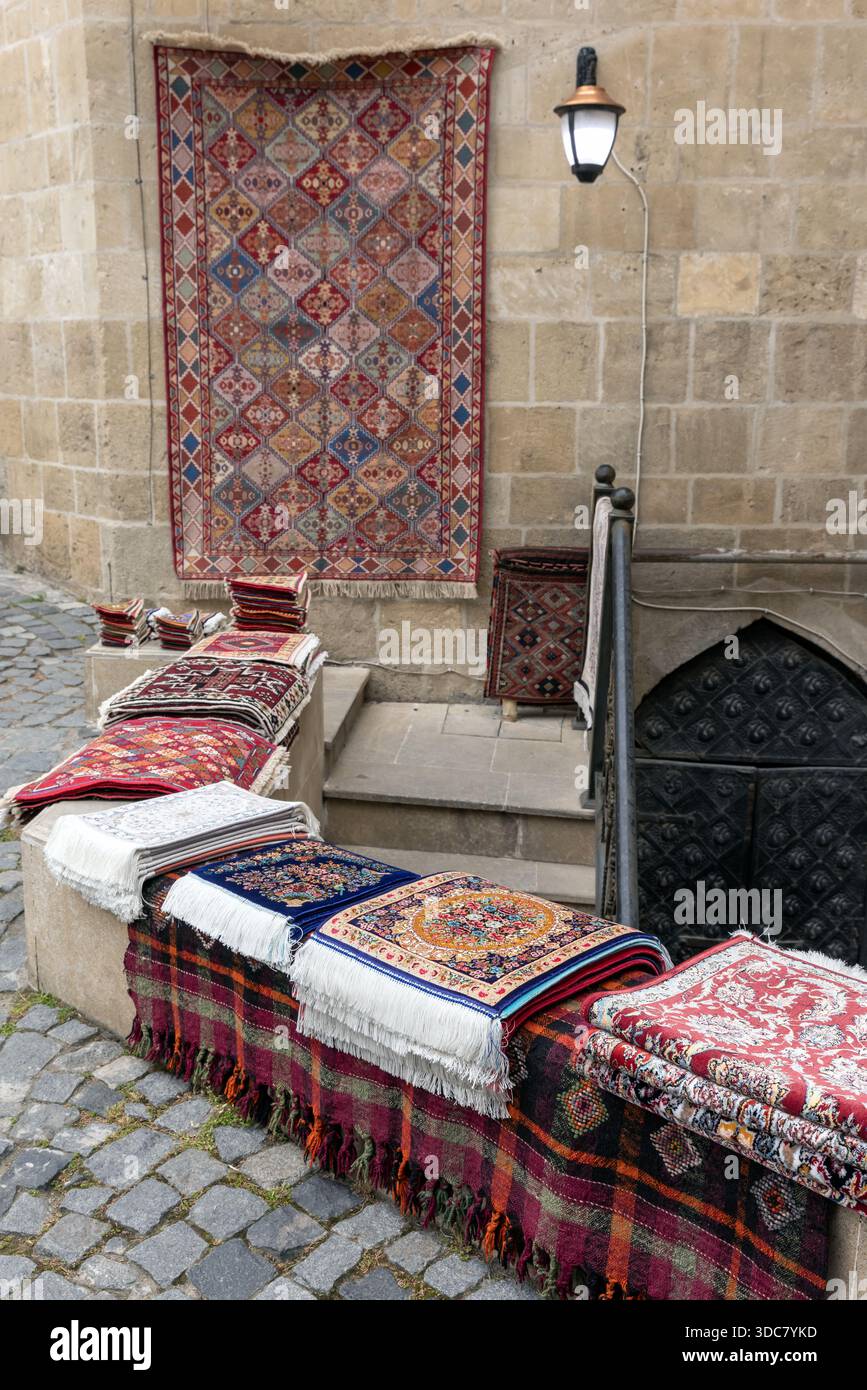 Collection vibrante de tapis et tapis faits à la main disposés à l'extérieur d'un bâtiment historique en pierre. Les motifs riches, les couleurs chaudes et les pompons évoquent le traditionnel Banque D'Images