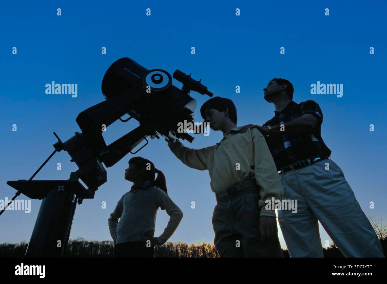 Une famille de trois personnes avec un télescope dans un champ ouvert au crépuscule. Ils se concentrent sur le ciel nocturne tout en partageant des connaissances sur l'astronomie et le plaisir Banque D'Images