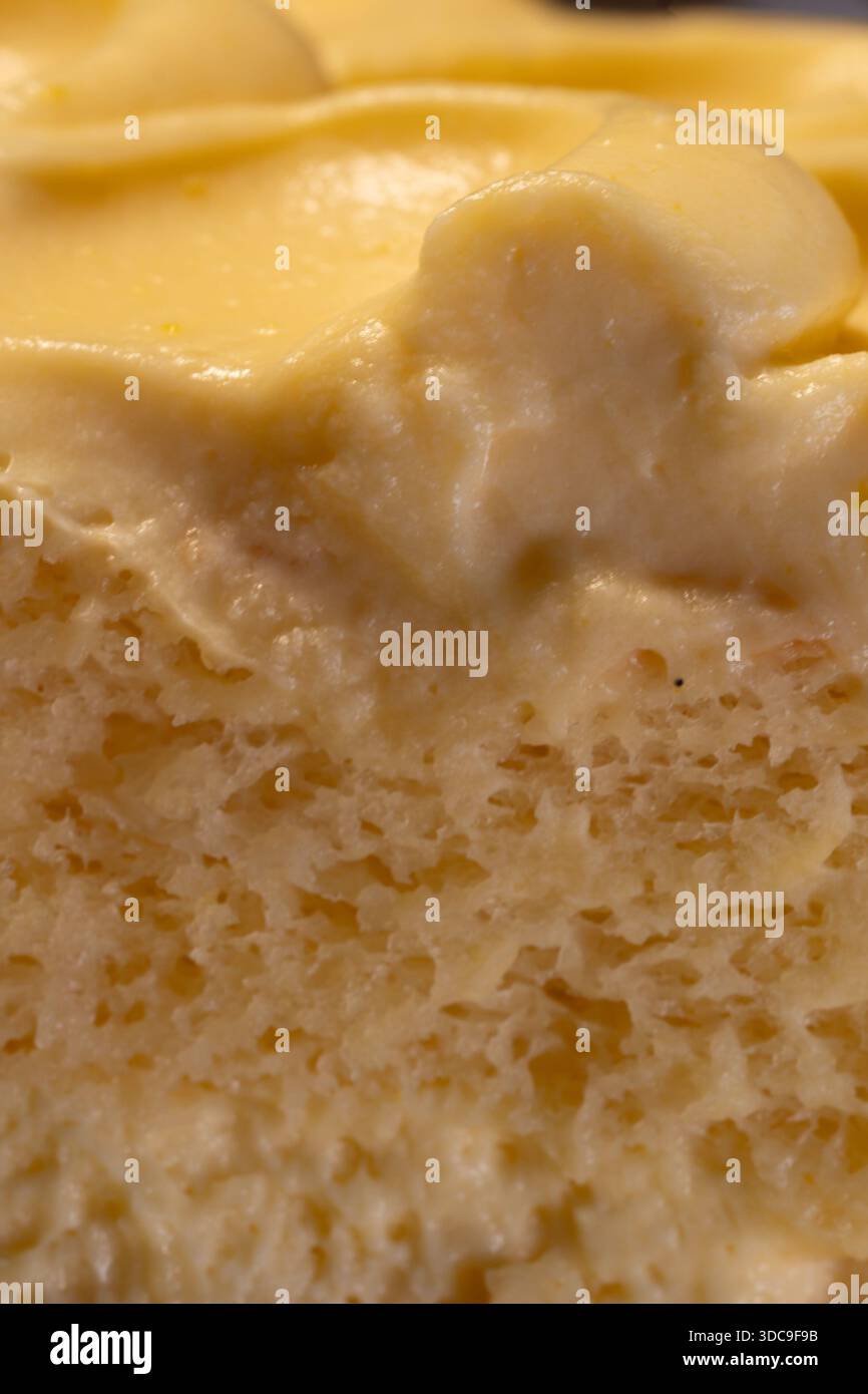 Gros plan détaillé d'un dessert jaune présentant sa garniture lisse et crémeuse et une couche de gâteau légère, aérée et texturée en dessous. Banque D'Images