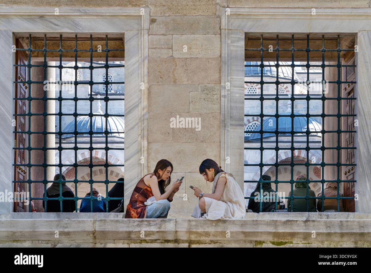 Deux femmes asiatiques au téléphone avec la femme musulmane en arrière-plan dans la cour de la Mosquée bleue à ISTA Banque D'Images