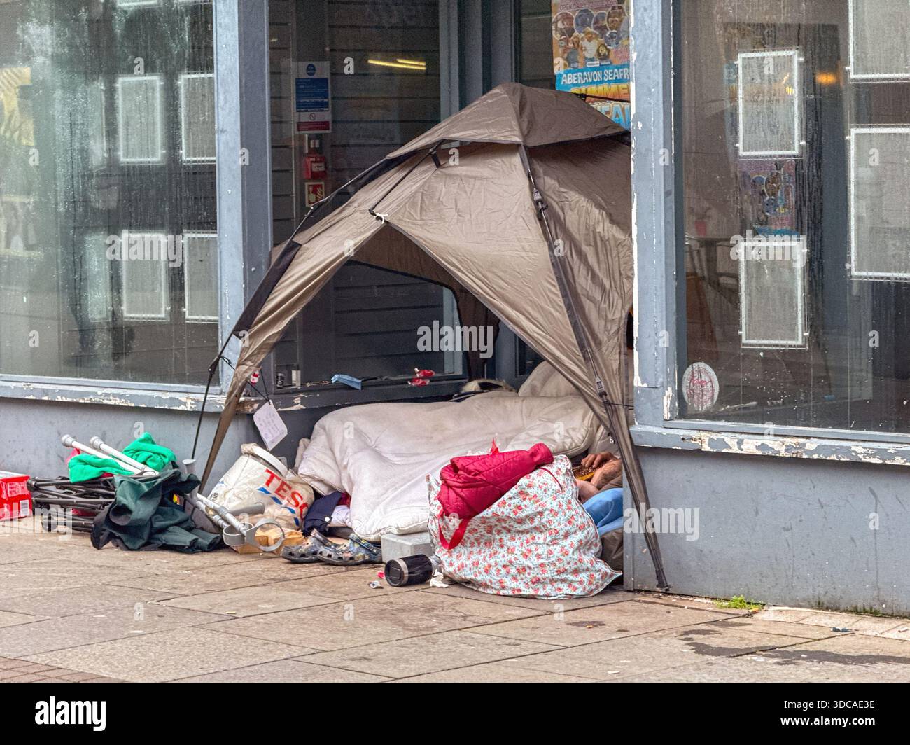 Bridgend, pays de Galles, Royaume-Uni - 14 décembre 2025 : tente et possessions d'un sans-abri sans-abri couchette dans l'entrée d'un magasin fermé dans le centre-ville de Bridgend. Banque D'Images