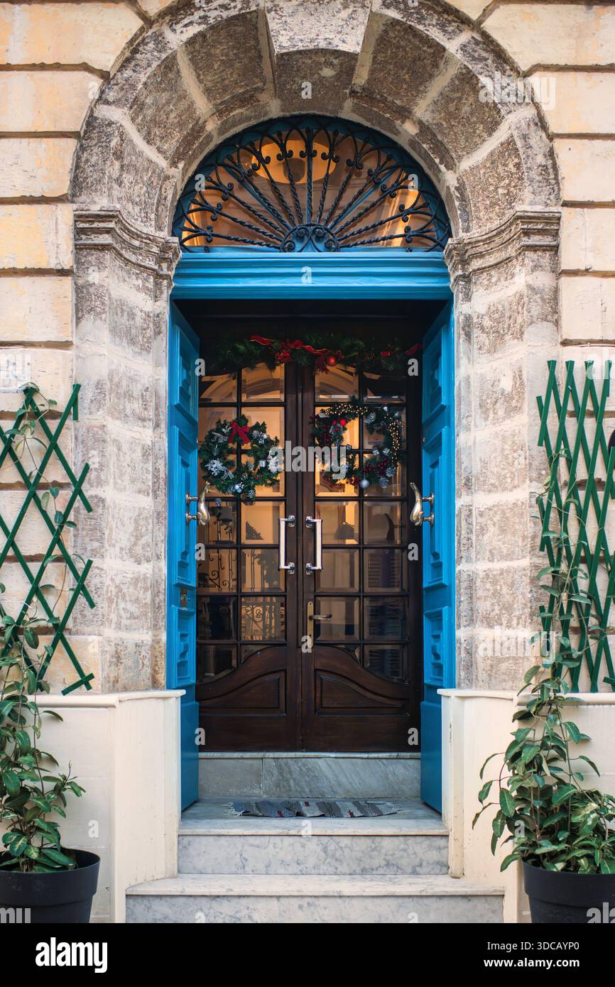 Entrée en pierre calcaire voûtée avec marches et plantes en pot décorées pour Noël avec des couronnes festives et des boules sur la façade en verre d'une porte en bois. Banque D'Images