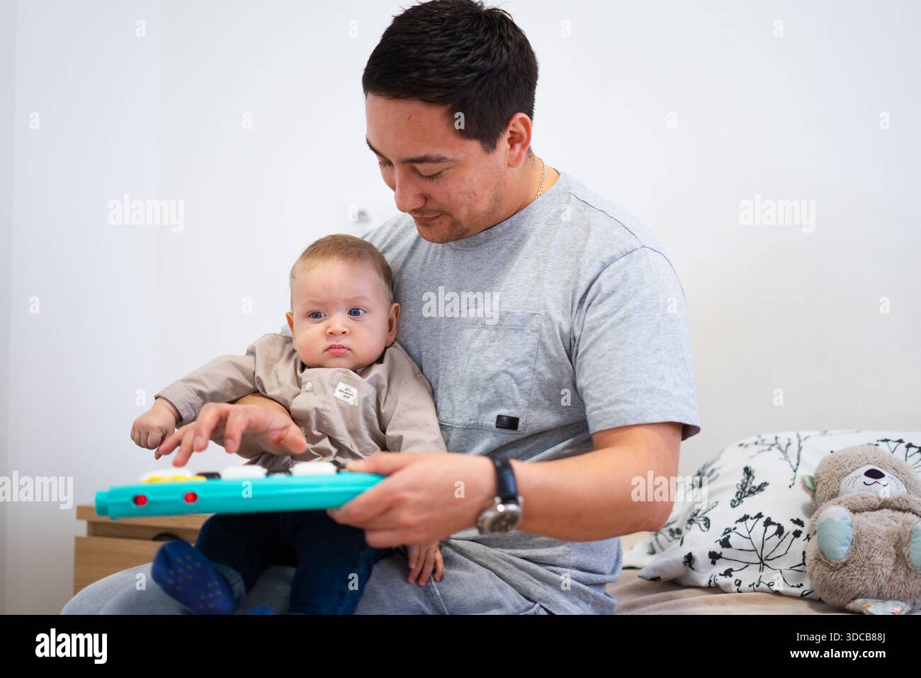Père tenant son bébé fils et l'aidant à jouer avec un piano jouet, favorisant le développement de la petite enfance et l'exploration musicale Banque D'Images
