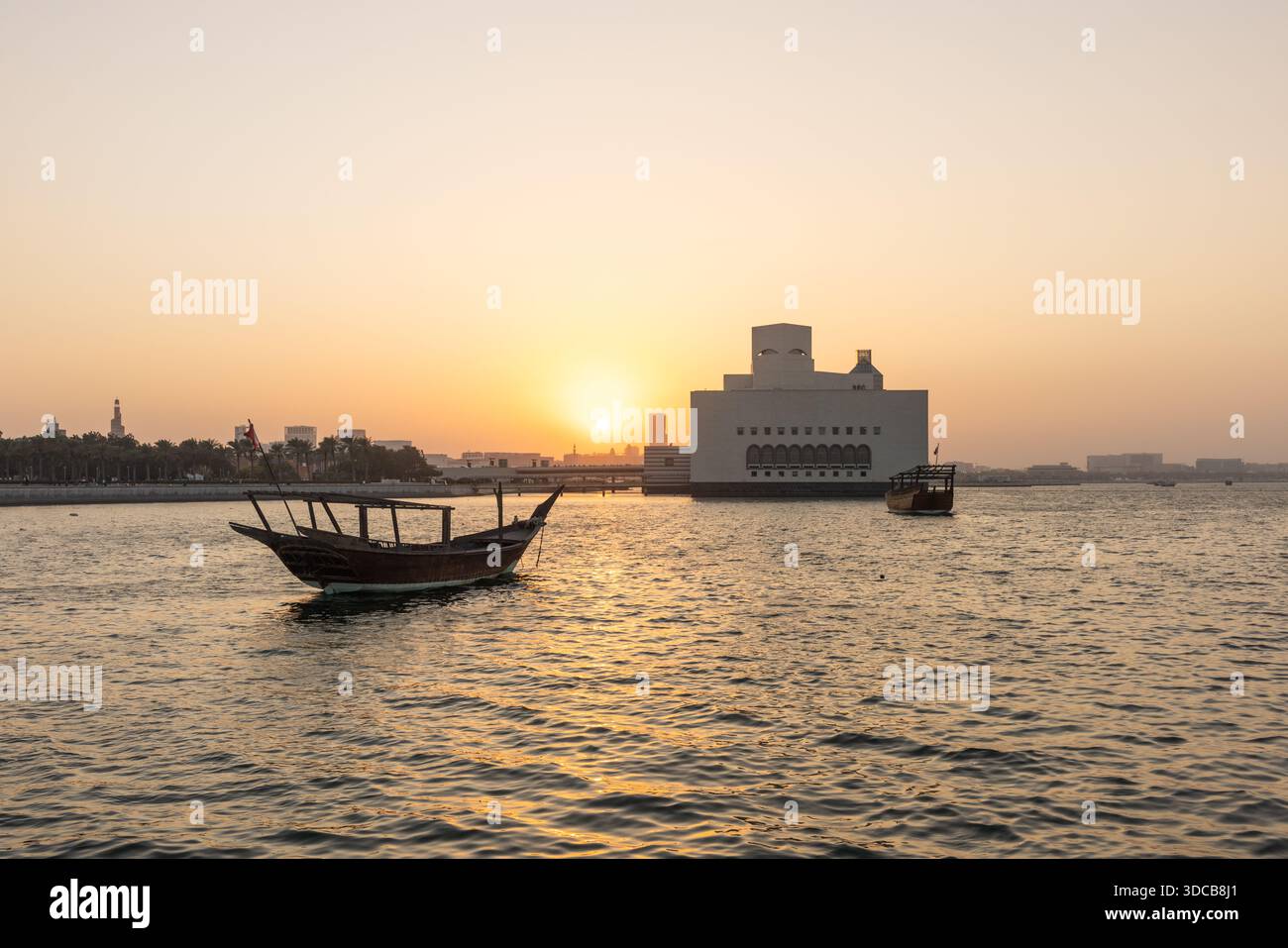 Croisière en boutre au coucher du soleil le long du port de Doha Corniche, avec bateaux traditionnels et vue sur les toits Banque D'Images