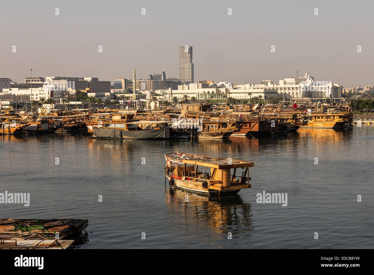 Croisière en boutre au coucher du soleil le long du port de Doha Corniche, avec bateaux traditionnels et vue sur les toits Banque D'Images