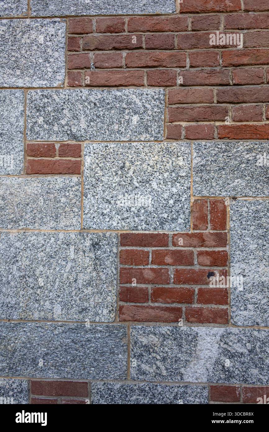 Un mur texturé composé de briques rouges et de blocs de granit gris crée une toile de fond urbaine audacieuse avec un contraste et une profondeur forts, adaptée à l'architecture, Banque D'Images